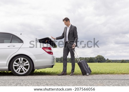 Full length of young businessman unloading luggage from broken down car at countryside