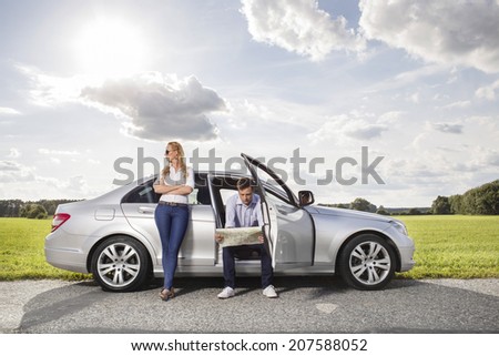 Full length of young woman looking away while man reading map in car at countryside
