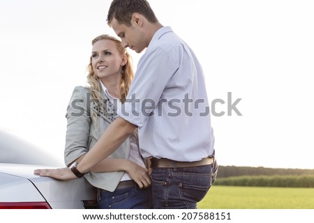 Romantic young couple leaning on back of car at countryside