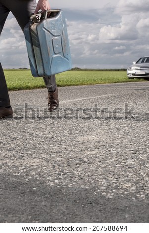 Low section of businessman carrying gasoline can with broken car in background at countryside