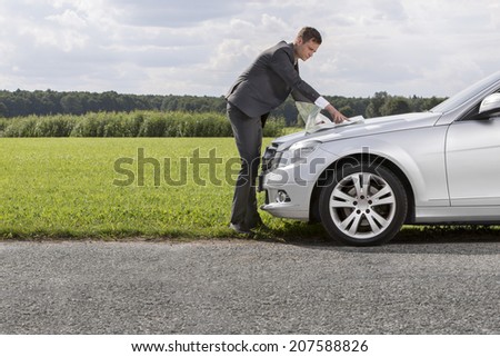 Full length side view of young businessman reading map on car hood at countryside