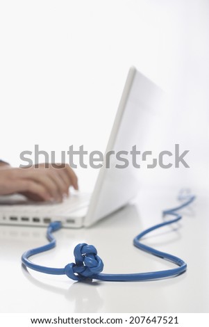 Closeup side view of hands using laptop with knotted cable against white background