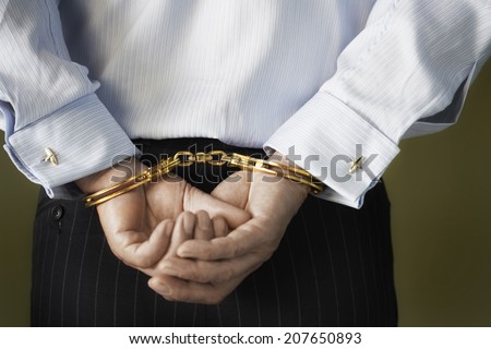 Closeup midsection of a businessman with hands cuffed behind back against green background