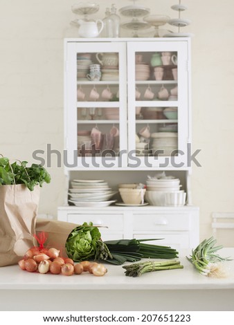 Closeup of fresh vegetables and paper bag on kitchen counter with utensils in cupboard
