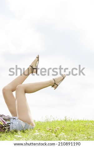 Low section of woman with feet up lying on grass against sky