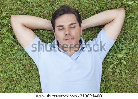 Young man with hands behind head lying on grass