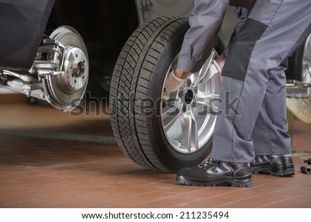 Low section of repairman fixing car\'s tire in repair shop