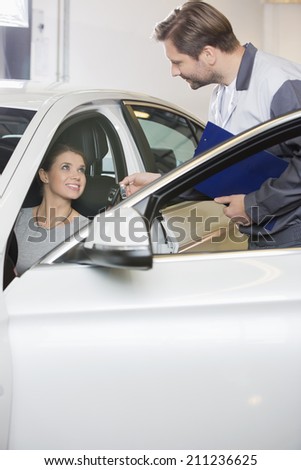 Automobile mechanic giving car key to female customer in repair shop