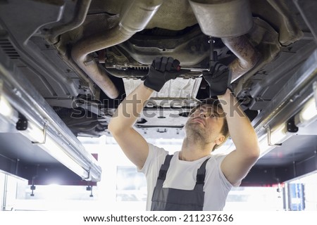 Mid adult automobile mechanic repairing car in workshop