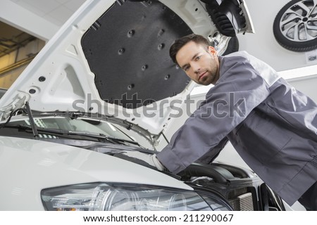 Portrait of confident male repair worker repairing car engine in repair shop