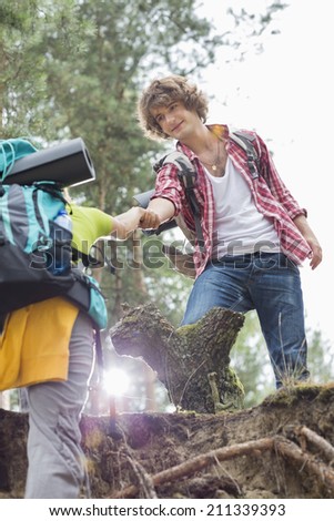 Low angle view of male hiker helping woman in climbing cliff at forest