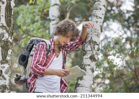 Backpacker reading map while leaning on tree trunk in forest