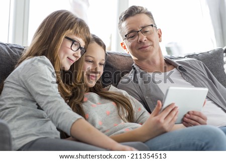 Father and daughters using tablet PC on sofa at home