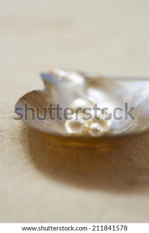 Four pearls in open oyster shell on beach close up