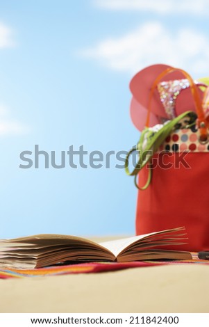 Open book next to beach bag on beach close up