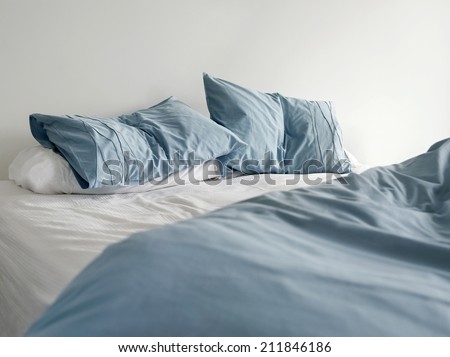 Morning view of an unmade bed with crumpled blue bed linens and no people