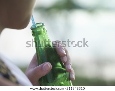 Closeup midsection of a young woman using straw to drink from a bottle against blurred background
