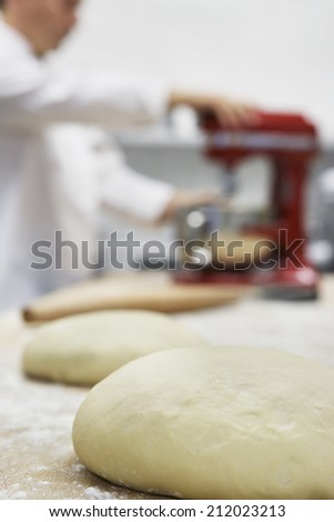 Side view of a blurred chef using dough mixer in kitchen with focus on dough in foreground
