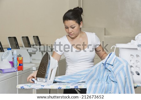 Young female employee ironing clothes in Laundromat