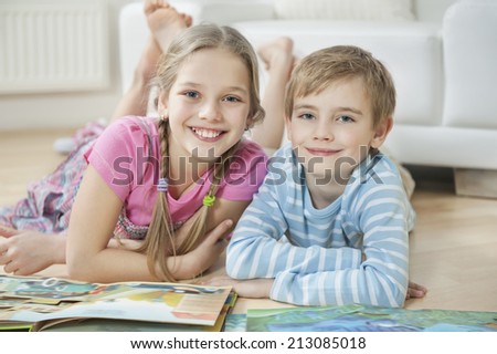 Portrait of happy brother and sister with story books while lying on floor