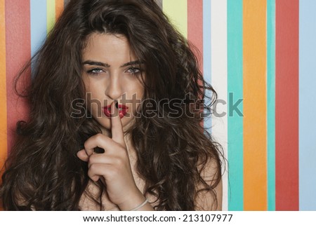 Portrait of a seductive young woman with finger on lips against colorful striped background