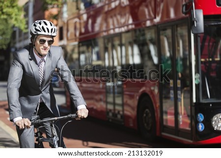 Young businessman riding bicycle by bus on street