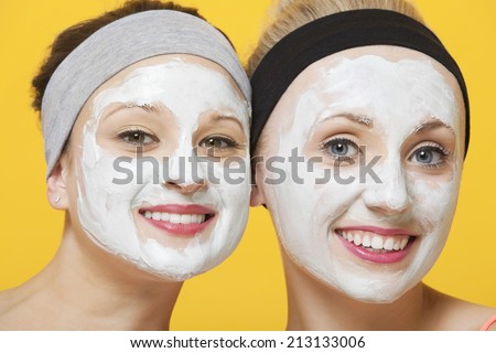 Portrait of two happy women with face pack on their faces over yellow background