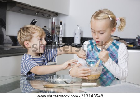 Happy brother and sister mixing batter together in kitchen