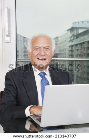 Portrait of happy elderly businessman with laptop sitting at table