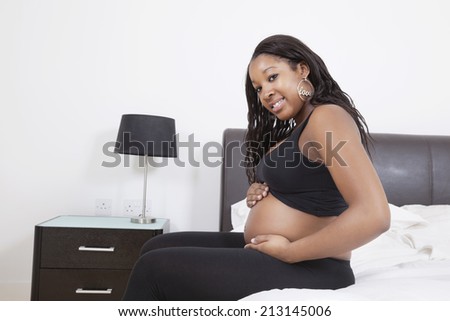 Portrait of happy young pregnant woman touching her belly in bed