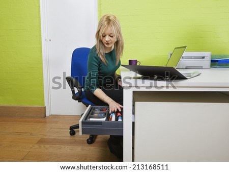 Young businesswoman searching something in drawer with laptop and file folder on desk