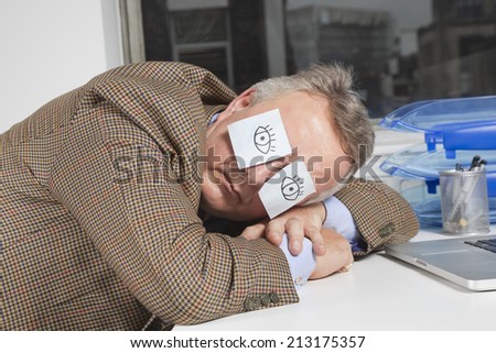 Businessman sleeping with sticky notes on eyes at desk in office