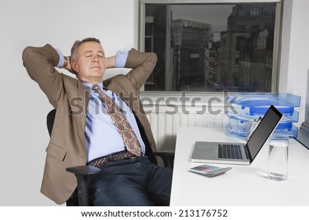 Middle-aged businessman resting on chair in front of laptop in office
