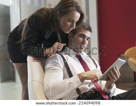 Businesswoman looking over male colleagues shoulder pointing at digital tablet