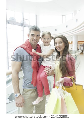 Father holding young girl posing with mother in shopping mall