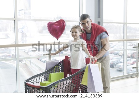 Father pushing young daughter in shopping trolley with shopping bags