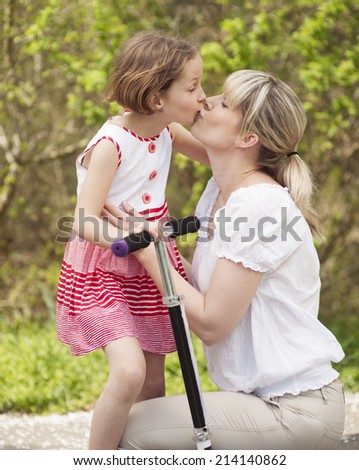 Mother and daughter kissing in park with scooter