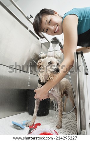 Portrait of young female animal groomer spraying water on dog