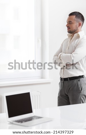 Businessman staring out of window with laptop in foreground