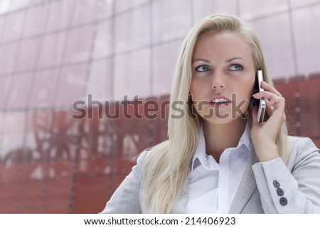 Close-up of young businesswoman communicating on mobile phone against office building