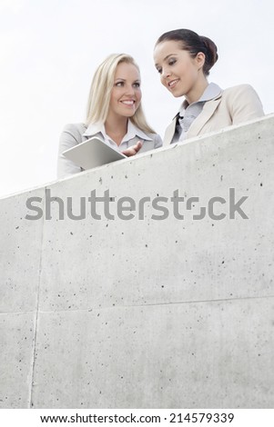 Low angle view of smiling business executives using digital tablet on office terrace against sky