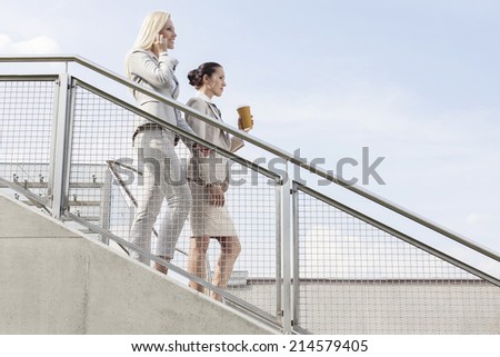 Profile shot of businesswomen moving down stairs against sky