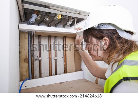 Female plumber examining pipes of central heating boiler