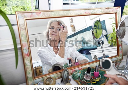 Mirror reflection of senior woman applying blusher at home