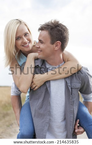 Happy young man giving piggyback ride to woman on field