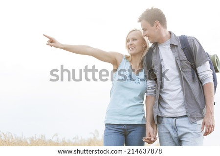 Happy female hiker showing something to man on field against clear sky