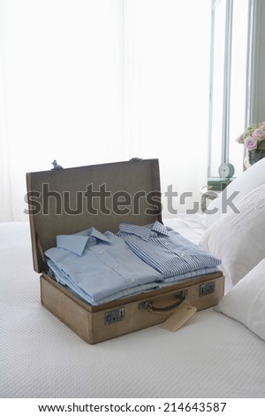 Ironed and folded shirts in open suitcase on bed