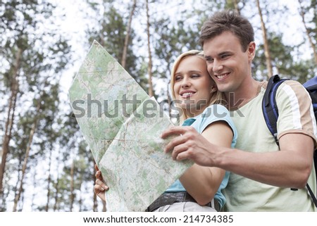 Happy young backpackers reading map in forest
