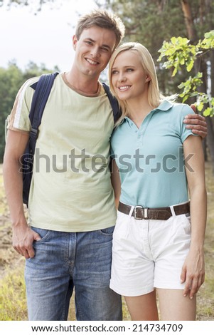 Portrait of happy man standing with woman while hiking in forest