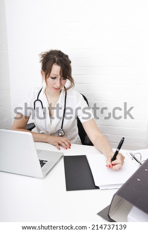 Young female doctor writing notes on desk in clinic